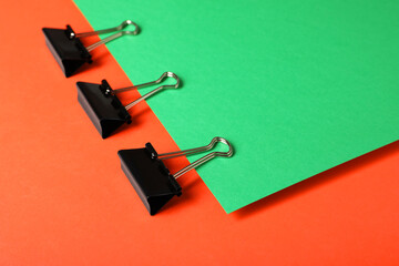 Black binder clips on color background. Stationery items