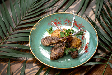 Plate with grilled meat t-bone on wooden table decorated with palm leaves. Horizontal format.