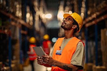 Warehouse worker using digital tablet looking up at tall shelves