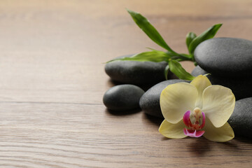 Fototapeta na wymiar Spa stones, beautiful orchid flower and bamboo sprout on wooden table. Space for text