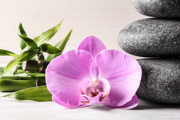 Fototapeta na wymiar Spa stones, bamboo and beautiful orchid flower on white table, closeup