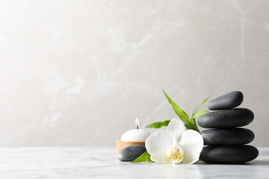 Spa stones, bamboo sprout, burning candle and beautiful orchid flower on white marble table, space for text