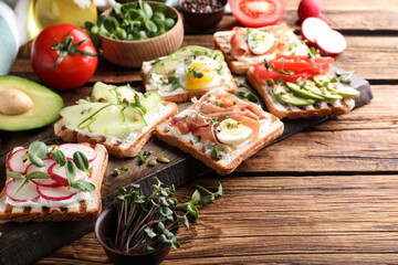 Different delicious sandwiches with microgreens on wooden table