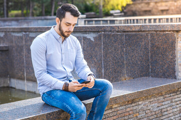 Obraz premium Portrait of a man businessman in a shirt with a beard who sits and uses a smartphone