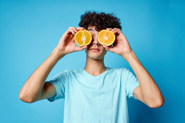guy with curly hair holding an orange fruit blue background