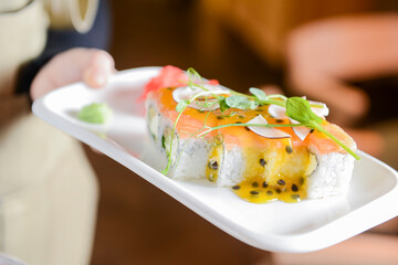 Sushi Set: sashimi and sushi rolls served in a white plate by waiter in restaurant. Eating out concept.