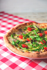 Prosciutto and Arugula Pizza with cherry tomatoes served on a white plate over red plaid table cloth.