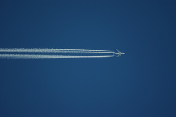 An airplane with contrails is silhouetted against the blue sky