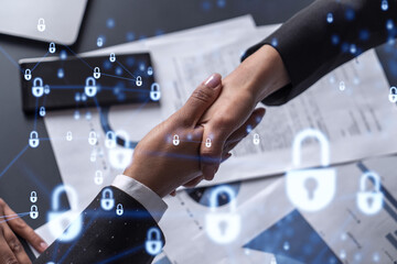 Handshake of two businesswomen who enters into the contract to protect cyber security of international company. Padlock Hologram icons over the table with documents.