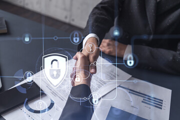 Fototapeta premium Handshake of two businesswomen who enters into the contract to protect cyber security of international company. Padlock Hologram icons over the table with documents.