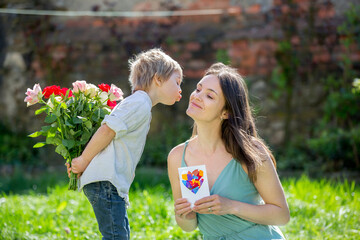 Obraz premium Beautiful kid and mom in spring park, flower and present. Mother getting gift from toddler boy for Mothers day