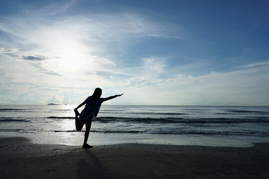 Silhouette of young woman practicing yoga on the beach at morning sun.