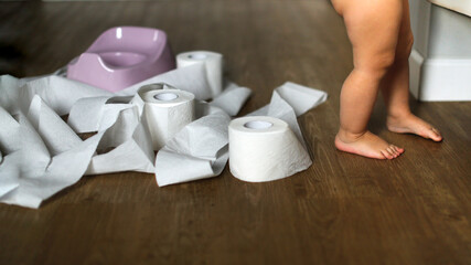 Funny kid Toddler sits on a pot with toilet paper, concept of teaching pot, child autonomy. Baby...