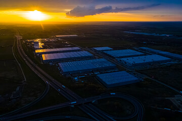 Fototapeta na wymiar Logistics park with warehouse, loading hub and many semi trucks with cargo trailers standing at the ramps for load and unload goods at sunset.