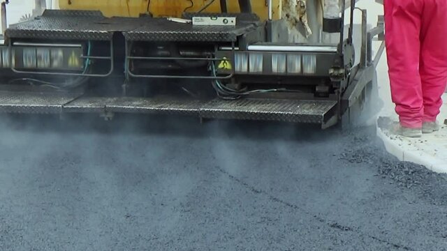 Close view on the workers and the asphalting machines. The heat of the burned propane create air turbulence near flame
