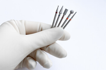 A pedicure specialist in white sterile gloves holds a set of professional diamond cutters for...