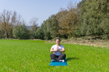 Curvy woman smiling practicing yoga on a mat on the grass with cobbler's pose