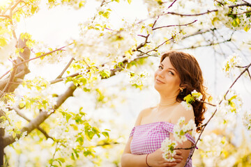 attractive woman near flowering tree in spring park. Cherry Orchard. solar glare