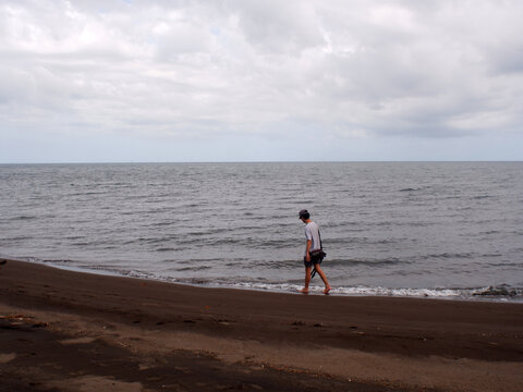 Young man walking barefoot aimlessly along a sandy seashore