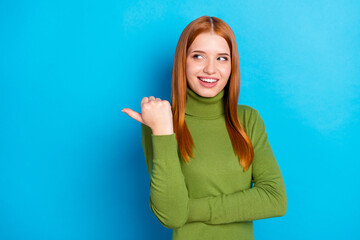 Photo of optimistic red hair lady point empty space wear green sweater isolated on blue color background