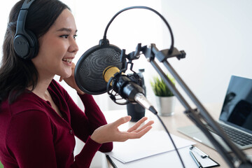 Bright Asian women record a podcast with a microphone and computer camera. A young woman working...
