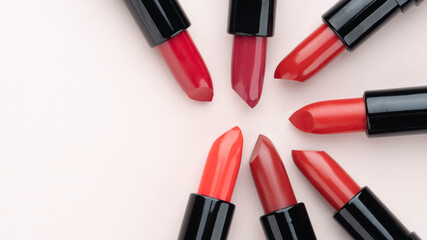 Red lipsticks of different shades arranged in a circle on beige background. Makeup and cosmetics concept. Close up. Flat layout. Copy space.