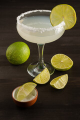 Top view of margarita cocktail glass with lime slices and salt, on wooden table with cut limes,...