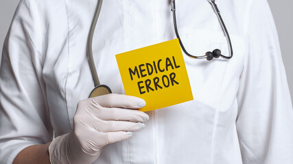 Cropped view of doctor in a white coat and sterile gloves holding a note with text - medical error