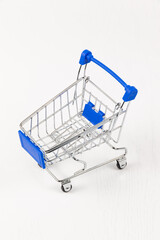 empty metal shiny grocery cart on wheels on white wooden table background