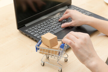 metal chrome trolley with boxes and female hands on the background of a black laptop on a wooden table. selective focus