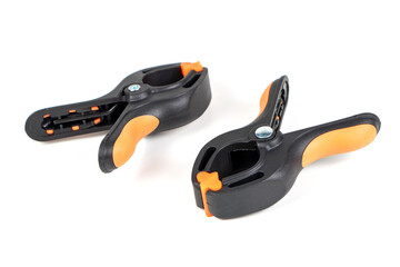 Obraz premium Plastic spring clamp isolated on white background. Clamping equipment. Working hand tool. Black and orange spring clamp. Closeup..