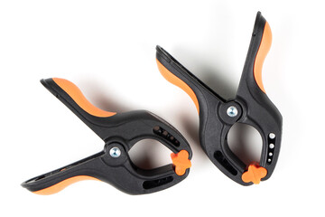 Obraz premium Plastic spring clamp isolated on white background. Clamping equipment. Working hand tool. Black and orange spring clamp. Closeup..