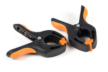 Obraz premium Plastic spring clamp isolated on white background. Clamping equipment. Working hand tool. Black and orange spring clamp. Closeup..