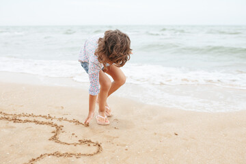 Five years cute curly caucasian girl painting on sand on the beach.