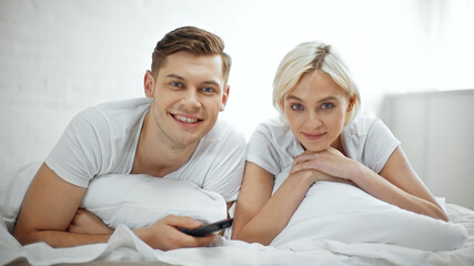 Fototapeta premium happy couple smiling while watching movie in bedroom