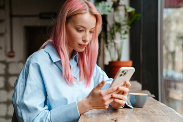 Young beautiful woman with pink hair using mobile phone in cafe - Powered by Adobe