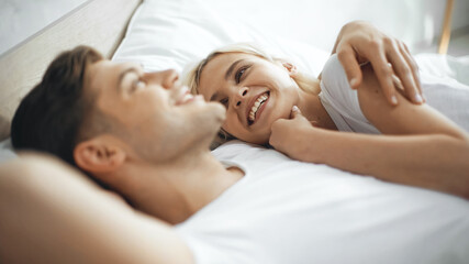 Fototapeta na wymiar happy woman smiling while lying on bed with boyfriend on blurred foreground