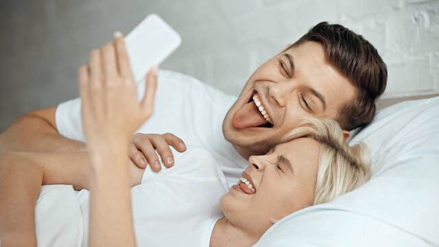happy young couple taking selfie on smartphone while sticking out tongues