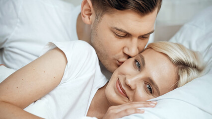 Obraz na płótnie Canvas young man kissing cheek of joyful girlfriend