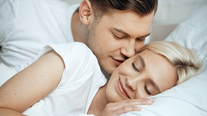Obraz na płótnie Canvas young man kissing cheek of cheerful blonde girlfriend