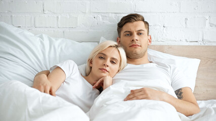 Obraz na płótnie Canvas tattooed man lying in bed with blonde girlfriend