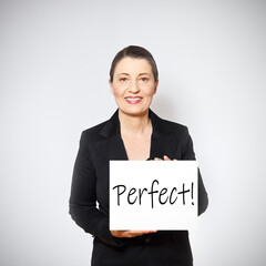 Smiling middle aged woman in black blazer holding up a sign with the praise: perfect, white...