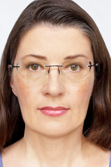 Biometric passport photo of a middle aged woman with long dark hair and glasses, neutral light...
