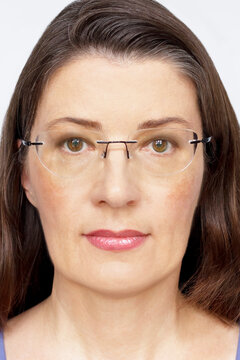 Biometric passport photo of a middle aged woman with long dark hair and glasses, neutral light background.