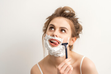 Beautiful young caucasian smiling woman shaving her face with razor sticking out tongue looking up...