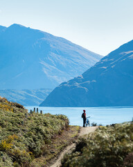 Fototapeta na wymiar Cyclist standing with his bike enjoying the views of the Lake Wanaka on Glendhu Bay track, South Island. Vertical format