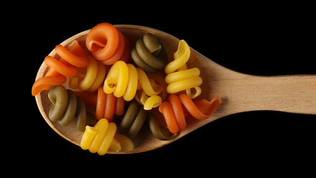 Pasta trottole tricolore made from durum wheat in wooden spoon isolated on black background, top view with clipping path