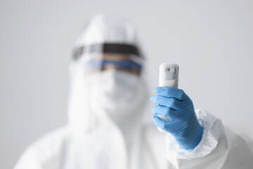 Doctor in protective anti-plague suit and screen holding infrared thermometer closeup