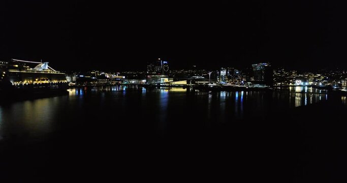 Aerial crane motion revealing Oslo city at night from illuminated Opera House