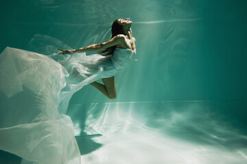 Fototapeta na wymiar brunette young woman in dress diving in pool